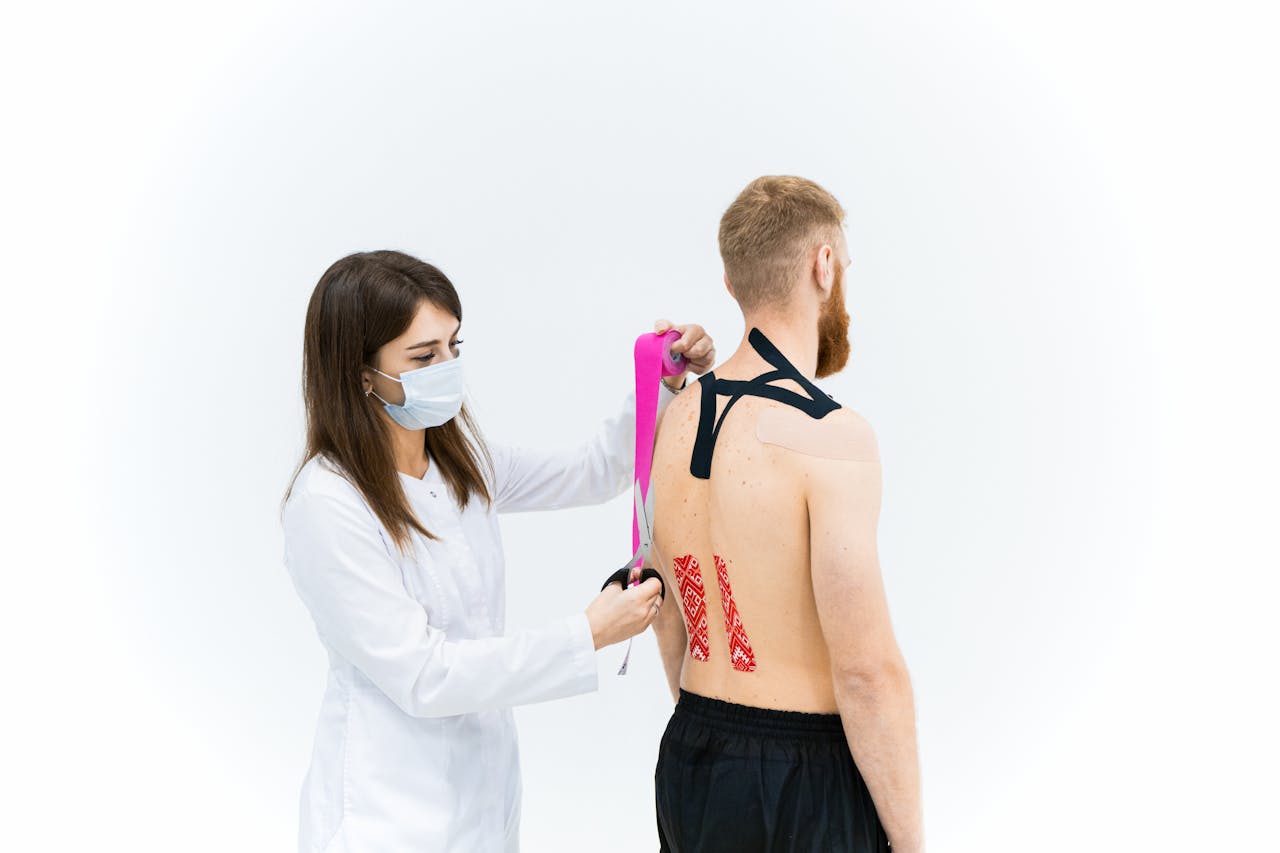 Medical practitioner applying kinesiology tape to a shirtless male patient's back.